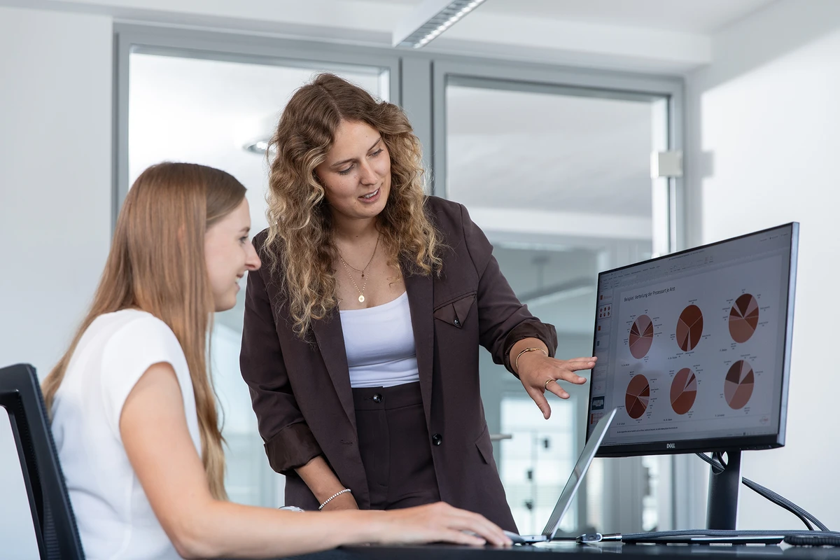 Zwei optimed-Mitarbeiterinnen analysieren gemeinsam Kennzahlenauswertungen auf einem Monitor. Karriere bei optimed: Mitarbeiterinnen analysieren Prozesskennzahlen – für alle, die medizinische Abläufe mit Daten verbessern möchten.
